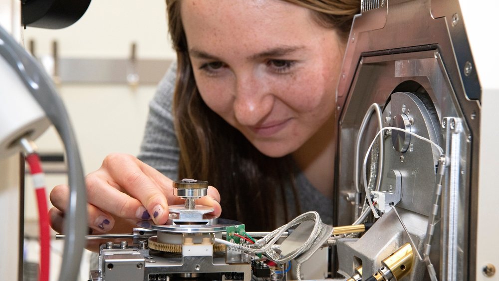 A student loading a sample into a scanning electron microscope