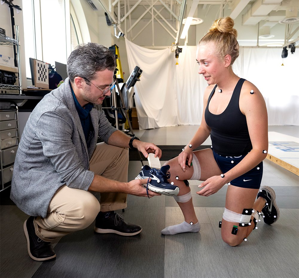Prof. Wheatley fitting a shoe on a student wearing motion-capture markers in the lab